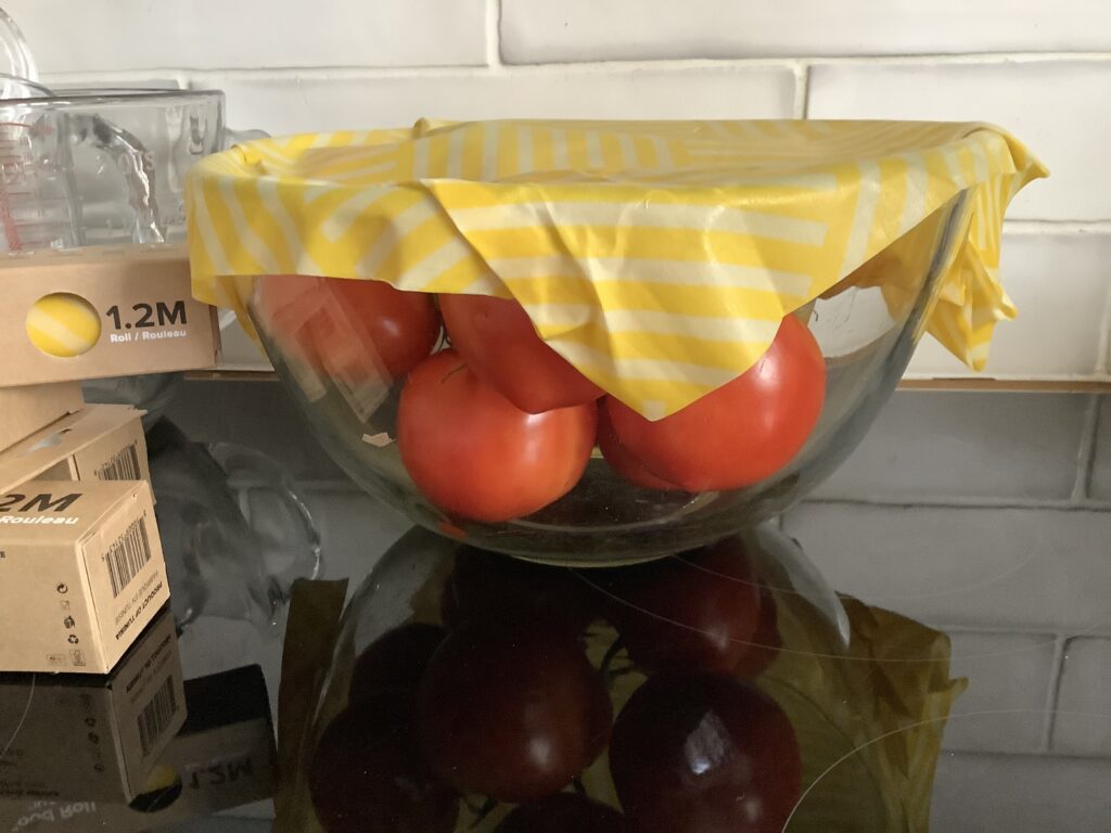 large bowl of red tomatoes covered with a cut to size piece of yellow and white bees was roll