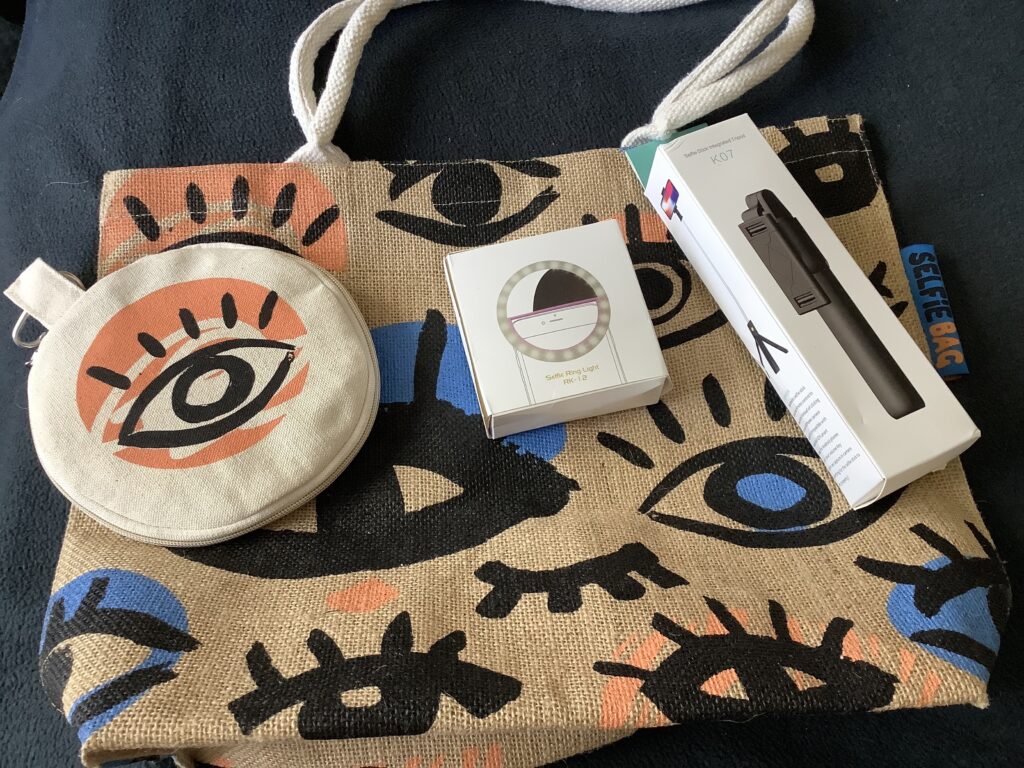 ute bag with handles with drawings of eyes along with selfie stick, selfie light and light diffuser