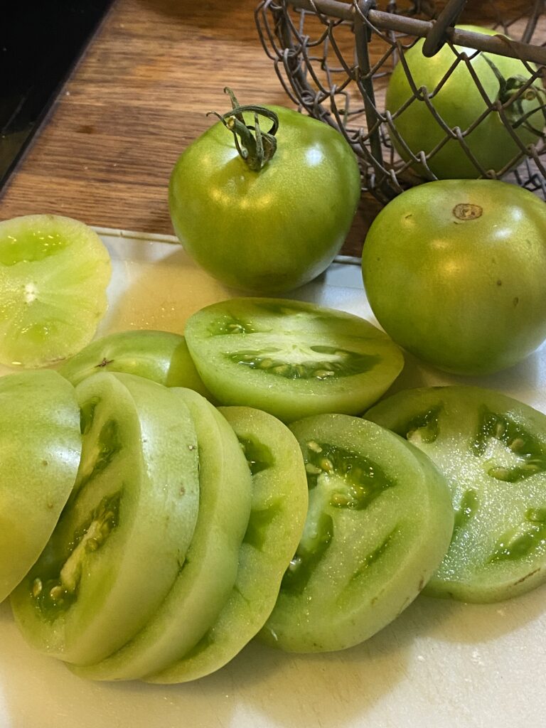Slices of green tomatoes with two whole tomatoes in the background