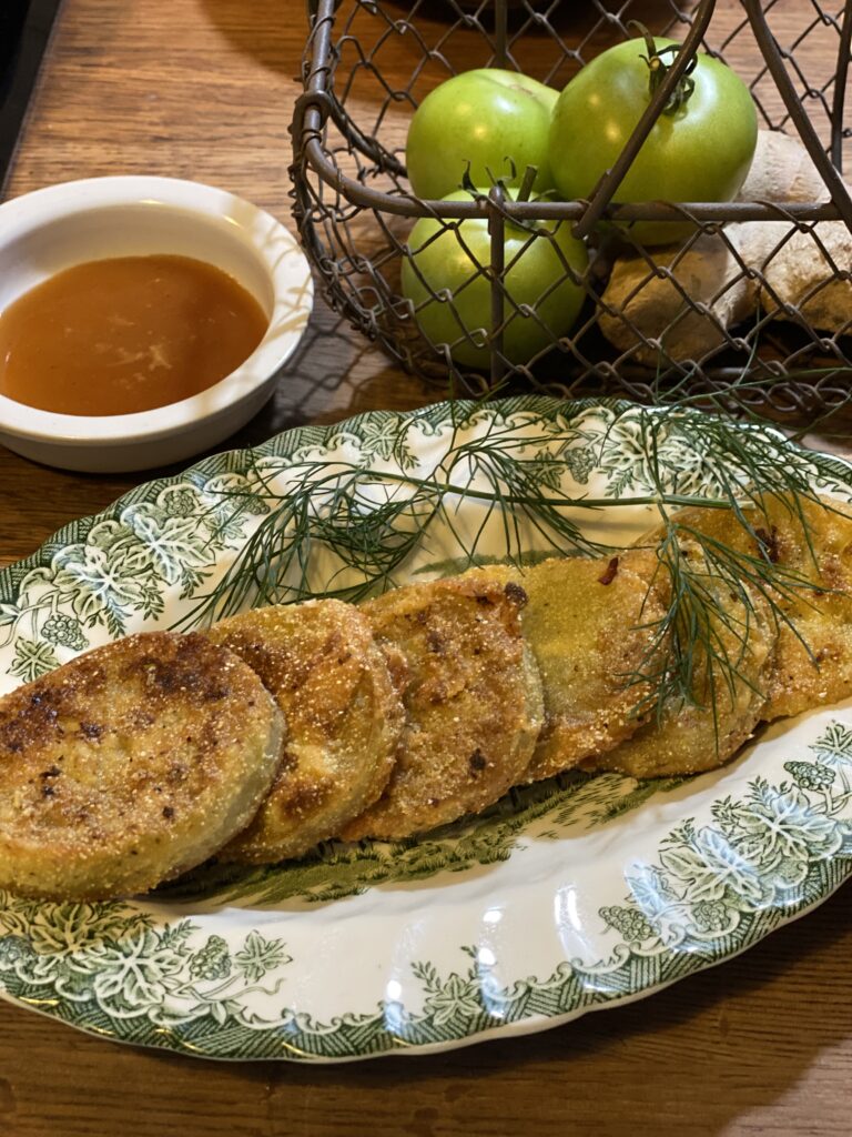 Green and white oval plate with slices of fried green tomatoes with a small white dish containing sweet and sour sauce for dipping