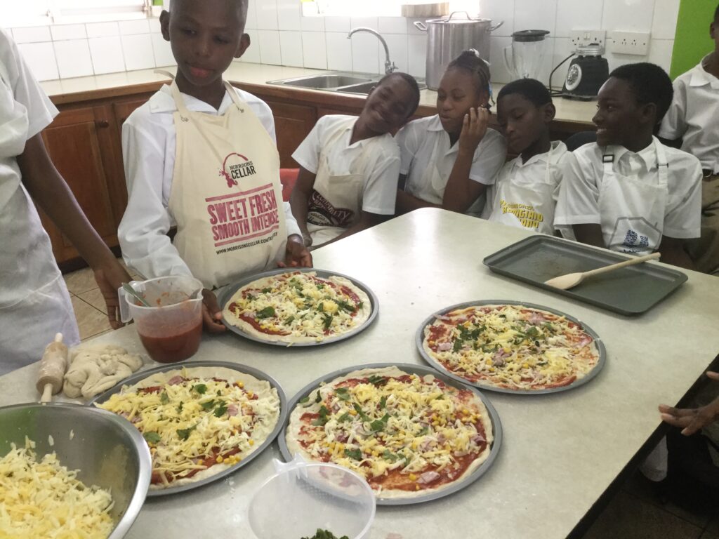 A student with four trays of pizza ready for the oven