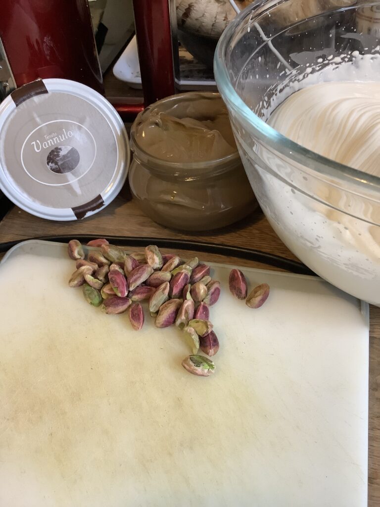 Pistachio cream with the lid off, bowl of creams and pistachios on a board.
